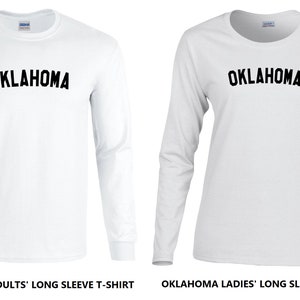 May include: Two white long-sleeve t-shirts with the word "OKLAHOMA" printed in black on the front. The shirt on the left is labeled "OKLAHOMA ADULTS' LONG SLEEVE T-SHIRT" and the shirt on the right is labeled "OKLAHOMA LADIES' LONG SLEEVE T-SHIRT".