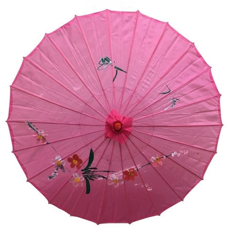 May include: A pink paper parasol with a floral and dragonfly design. The parasol is closed and has a wooden handle.