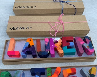 May include: Two brown cardboard boxes with the names "DOMINIC" and "ALESSIA" written on them.  Two boxes contain colourful crayon letters spelling out the names "LAUREN" and "MIKEY".