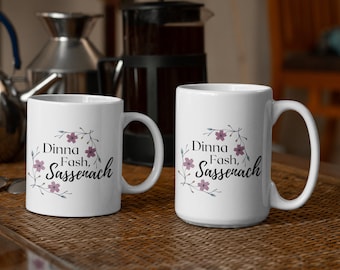 May include: Two white ceramic mugs with a floral design and the text "Dinna Fash, Sassenach".