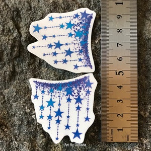 K&ouml;nnte beinhalten: Zwei wei&szlig;e Aufkleber mit blauem Sternmuster. Die Aufkleber haben einen gezackten Rand und zeigen Str&auml;nge aus blauen Sternen mit einem blauen Glitzerrahmen. Ein Lineal zeigt Messungen in Millimetern. Der Text "Art By Octavia" befindet sich unten.