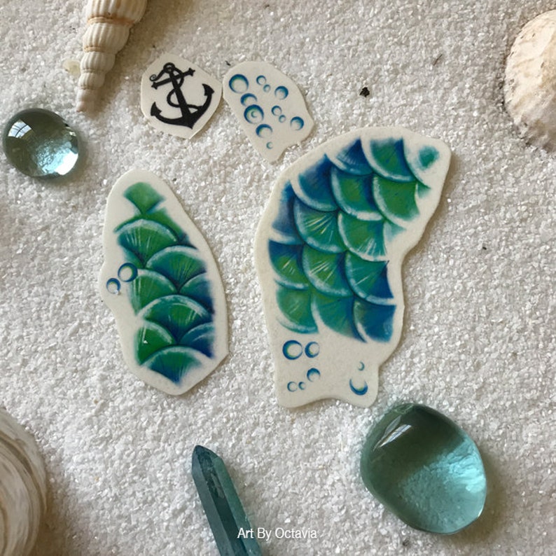 May include: A set of four temporary tattoos featuring a mermaid tail, bubbles, and an anchor. The tattoos are printed on white paper and are ready to be applied to skin.