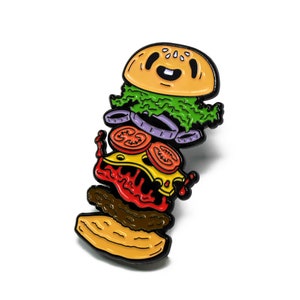 Puede incluir: Un pin de esmalte colorido de una hamburguesa de dibujos animados con un bollo sonriente, lechuga, cebolla, tomate, queso y una salsa roja que gotea. La hamburguesa está apilada al revés.