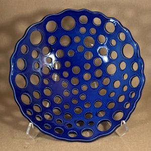 May include: A vibrant blue ceramic bowl with a unique perforated design. The bowl features numerous circular holes of varying sizes, creating an open, airy aesthetic. The rim has a wavy edge, adding to its decorative appeal. This bowl is a striking piece of home decor.