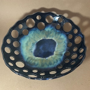 May include: A decorative ceramic bowl with a unique design. The bowl is dark blue with a textured, openwork rim and a central opening. The interior features a blend of blue and green hues, creating a striking visual effect.