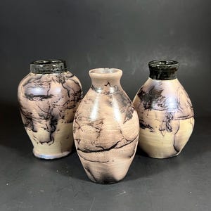 May include: Three handcrafted ceramic vases with a unique, textured design. The vases feature a light beige base with striking black and brown patterns, and dark rims. The vases are of varying sizes and shapes, perfect for home decor.