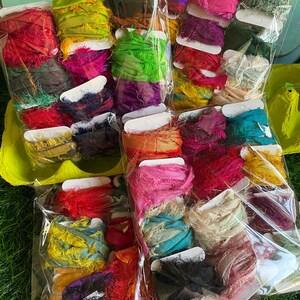May include: A collection of colorful, textured ribbon spools in various shades of red, pink, green, yellow, and blue. The spools are packaged in clear plastic bags, showcasing the vibrant colors and frayed edges of the ribbon. Ideal for crafting and embellishments.