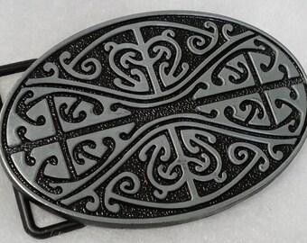 May include: A silver-toned belt buckle with a black and silver design. The design is a repeating pattern of swirls and curves.