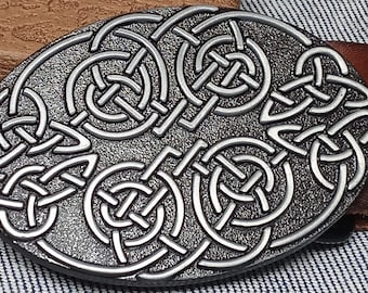 May include: Silver-toned belt buckle with a Celtic knot design. The buckle is oval-shaped and has a detailed, intricate pattern.
