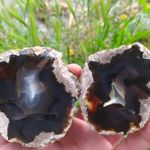 Könnte beinhalten: Zwei Hälften einer Achat-Geode mit einem dunkelbraunen und weißen Inneren. Die Geodenhälften liegen auf einer Hand.