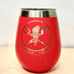 May include: Red stainless steel wine tumbler featuring a gold logo of a torch, crossed swords, and lightning bolts. The logo also includes the text "VAW - 125". The tumbler has the word "YETI" embossed on the bottom.