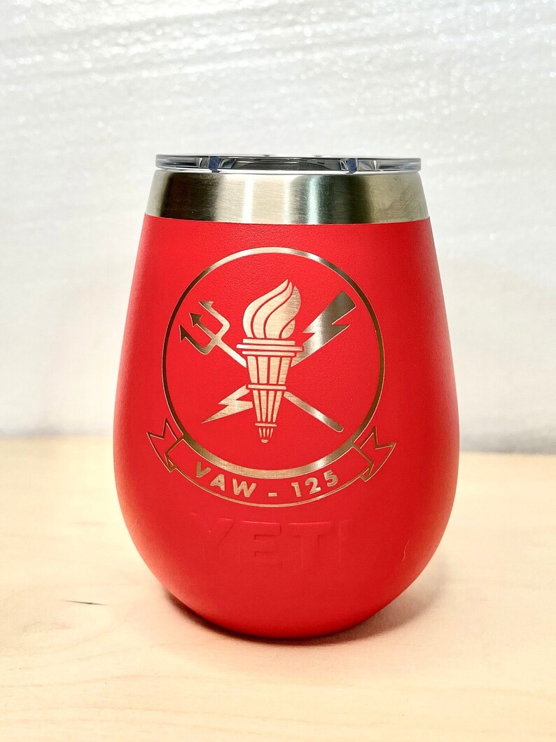 May include: Red stainless steel wine tumbler featuring a gold logo of a torch, crossed swords, and lightning bolts. The logo also includes the text "VAW - 125". The tumbler has the word "YETI" embossed on the bottom.