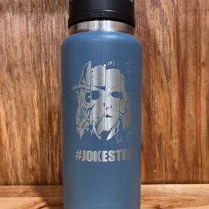 May include: A blue Yeti water bottle with a stainless steel lid and a black handle. The bottle features a laser-etched design of a horror movie character with the text "#JOKESTER" underneath.