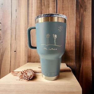 May include: A blue Yeti tumbler with a gold inscription that reads "Mrs. LeMaire" and a child's drawing of two stick figures and a sun.