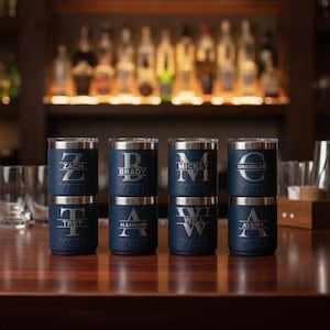 Peut inclure: Huit gobelets en acier inoxydable bleu marine empilés en deux colonnes de quatre. Chaque gobelet présente une lettre monogramme gravée en argent avec un nom centré horizontalement et le logo YETI imprimé à la base.