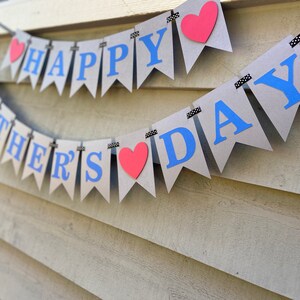 May include: A brown paper banner with the words "Happy Father's Day" in blue letters and red hearts. The banner is strung with black and white ribbon.