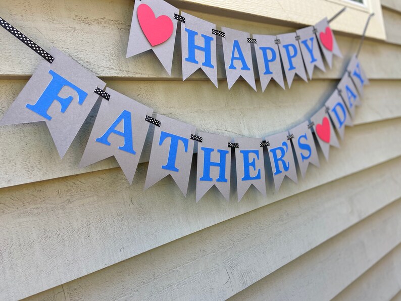 May include: A gray and blue banner with the text "Happy Father's Day" and red hearts. The banner is strung on a black and white string.