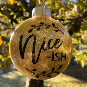 May include: Gold glitter Christmas bauble with black lettering that reads "Nice-ish".