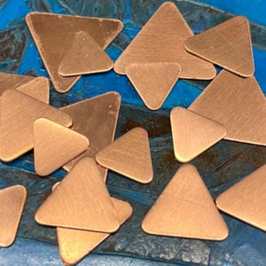 May include: A collection of small, triangular copper shapes with a brushed finish. The copper triangles are scattered on a blue surface.