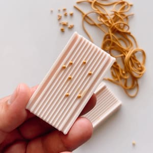 Peut inclure: Deux barres de savon rectangulaires roses avec des paillettes dorées sur le dessus. Les barres de savon ont une texture côtelée.