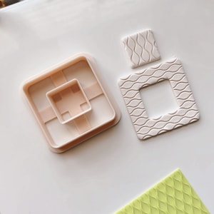 May include: A set of three polymer clay molds for making miniature perfume bottles. The molds are in the shape of a square with a smaller square inside. The molds are white and have a textured surface. The molds are on a white surface.