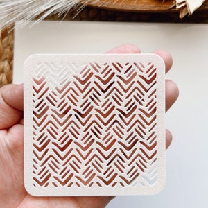 May include: White plastic stencil with a repeating chevron pattern. The stencil is designed for crafting and decorating.