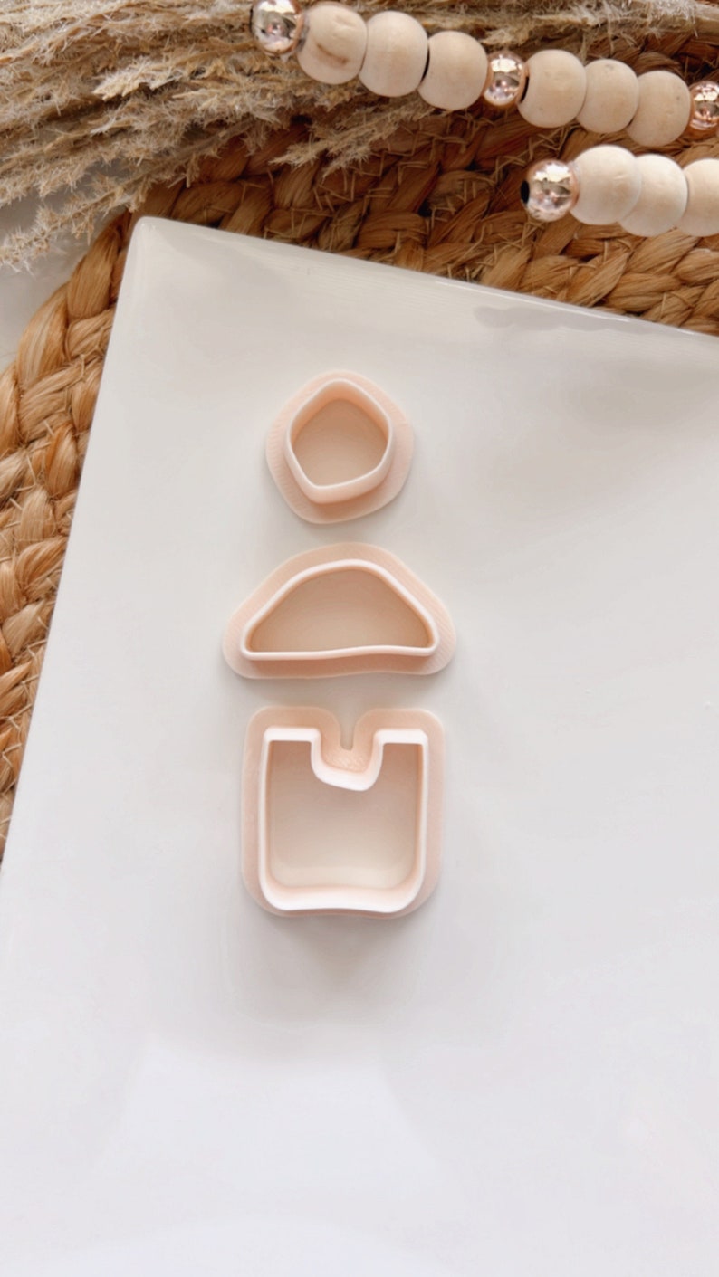 Puede incluir: Tres cortadores de galletas de pl&aacute;stico rosa en forma de c&iacute;rculo, semic&iacute;rculo y rect&aacute;ngulo. Los cortadores est&aacute;n dispuestos verticalmente sobre una superficie blanca.