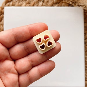 May include: A white plastic mold with four heart-shaped cutouts. The mold is designed for making cookies or other treats.