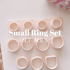 Puede incluir: Un juego de 9 moldes de anillos de plástico rosa para hacer joyas. Los moldes están etiquetados con los tamaños 7, 7.5, 8 y 8.5. El texto "Small Ring Set N.7-N.8.5" está impreso en la superficie blanca.