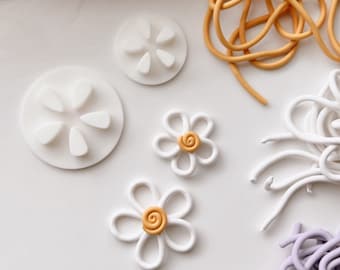 May include: White polymer clay flower shapes with yellow centers, white polymer clay flower cutters, and white, yellow, and purple polymer clay strands.