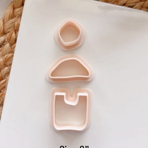 Puede incluir: Tres cortadores de galletas de pl&aacute;stico rosa en forma de c&iacute;rculo, semic&iacute;rculo y rect&aacute;ngulo con un recorte. Los cortadores est&aacute;n dispuestos verticalmente sobre una superficie blanca. Tama&ntilde;o: 5 cm