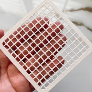 May include: White square stencil with a grid pattern. The stencil is made of a thin, flexible material and has a smooth surface.