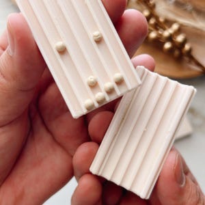 May include: Two white rectangular soap bars with raised lines. One bar has small white dots on the surface.