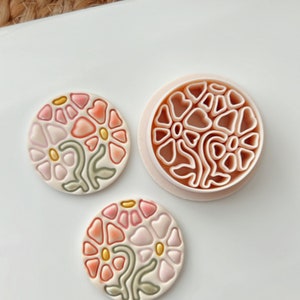 Puede incluir: Dos posavasos de cerámica rosa y blanca con un diseño floral y un molde a juego para hacer los posavasos.