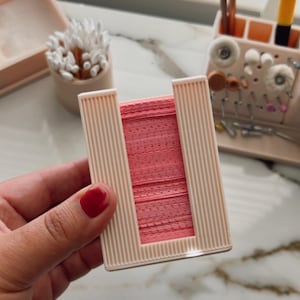 Puede incluir: Un contenedor de plástico rosa con una ranura para guardar esponjas de maquillaje. El contenedor tiene un diseño texturizado y está hecho de un material duradero.