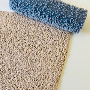 Puede incluir: Una superficie rectangular texturizada, de color marrón claro, con un rodillo azul con cerdas en la parte superior. El rodillo tiene forma rectangular y está cubierto de pequeñas protuberancias puntiagudas. La superficie tiene una textura porosa y desigual.