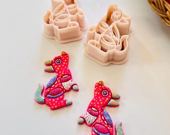 May include: Two pink plastic cookie cutters and two colorful, decorated bird-shaped ornaments. The ornaments are pink with yellow polka dots, blue and white accents, and a red and yellow design. The cookie cutters are light pink.