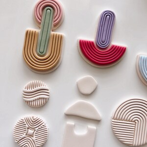 Puede incluir: Un conjunto de moldes de arcilla polim&eacute;rica para crear formas geom&eacute;tricas. Los moldes son de varios colores, incluyendo rosa, morado, verde y rojo. Los moldes est&aacute;n dispuestos sobre una superficie blanca.