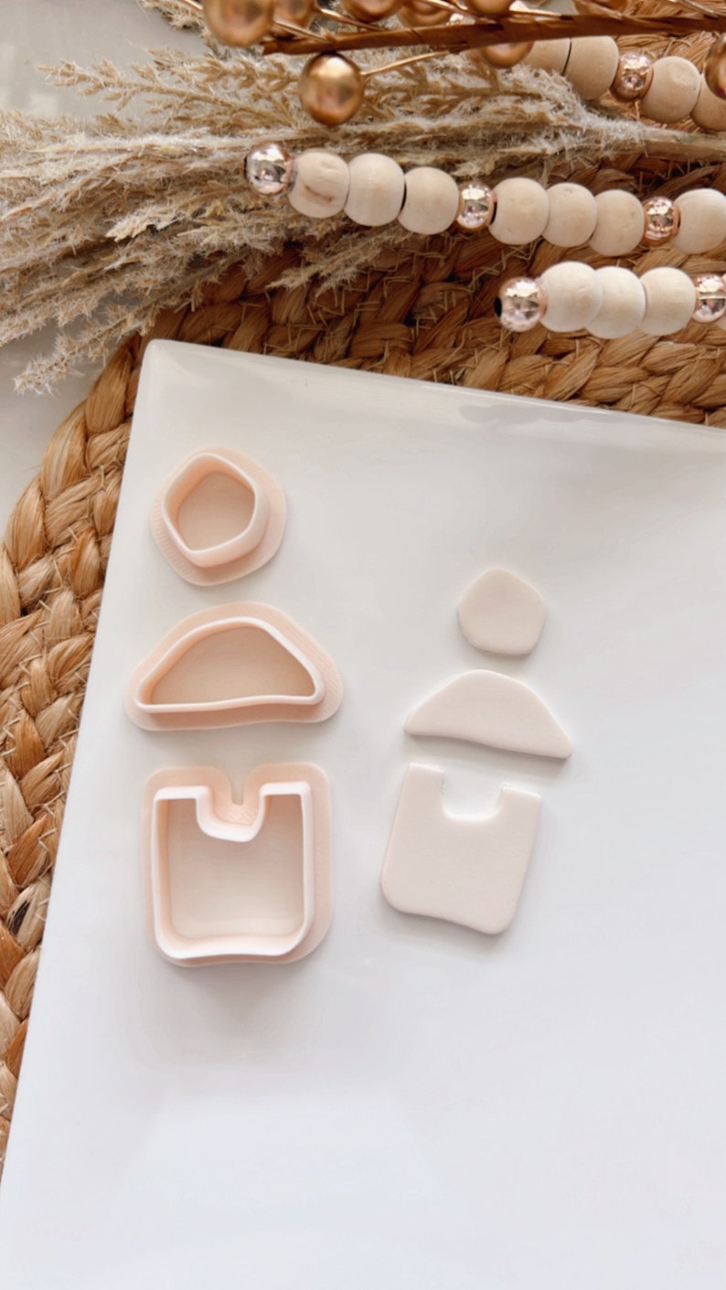 Puede incluir: Un juego de cuatro cortadores de galletas con forma de figuras geom&eacute;tricas abstractas. Los cortadores est&aacute;n hechos de pl&aacute;stico rosa claro y est&aacute;n dispuestos sobre una superficie blanca.