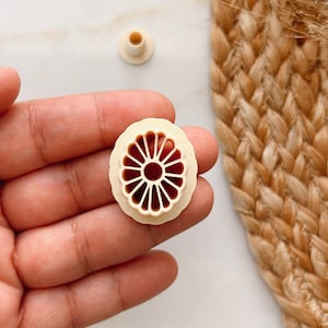 Puede incluir: Primer plano de un círculo decorativo de plástico blanco con un diseño detallado e intrincado. El círculo tiene un centro grande abierto y un centro cerrado más pequeño.