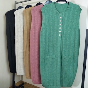 Può includere: Cinque gilet senza maniche in maglia appesi a un rack. I gilet sono in nero, beige, marrone, rosa e verde. Il gilet verde ha una chiusura con bottoni.