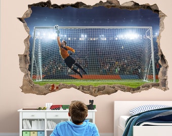 May include: A young person sits on a green and white striped rug, watching a football player make a save in a stadium. The football player is wearing a blue and orange kit and is diving to catch the ball. The image is a wall decal that creates the illusion of a hole in the wall.