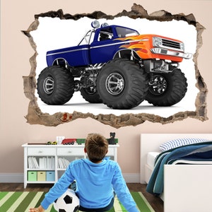 May include: A blue and orange monster truck with large tires is shown in a wall decal. The decal is designed to look like the truck is breaking through the wall.