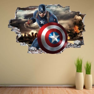 Peut inclure: Un autocollant mural repr&eacute;sentant Captain America per&ccedil;ant un mur. L'image montre Captain America dans son costume bleu, blanc et rouge, tenant son bouclier. L'arri&egrave;re-plan repr&eacute;sente une ville attaqu&eacute;e avec des explosions et des nuages sombres.
