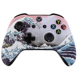 Puede incluir: Un mando de Xbox rosa y blanco con un diseño negro y azul de la Gran Ola de Kanagawa.