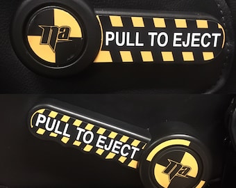 May include: Two black handles with yellow and black striped warning labels that say "PULL TO EJECT". Each handle has a black and yellow target with the letter "na" in the center.