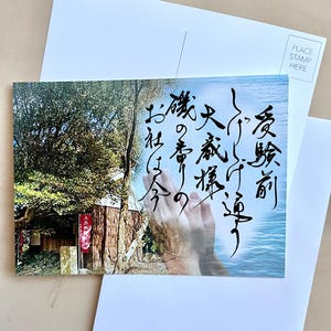 以下が含まれることがあります： 日本の寺院の風景が描かれた絵はがき。緑豊かな木々と水辺が特徴で、日本語の書道が施されています。2枚の白い無地の絵はがきの上に置かれています。