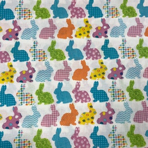 Puede incluir: Tela blanca con un patr&oacute;n repetido de conejos de patchwork de colores. Los conejos son de varios colores, incluyendo rosa, azul, verde, naranja y amarillo.