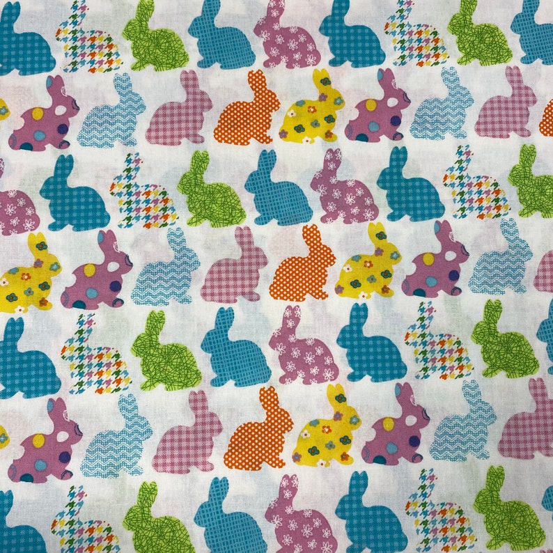 Puede incluir: Tela blanca con un patr&oacute;n repetido de conejos de patchwork de colores. Los conejos son de varios colores, incluyendo rosa, azul, verde, naranja y amarillo.