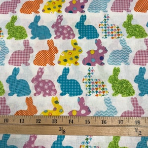 Puede incluir: Tela blanca con un patr&oacute;n repetido de siluetas de conejos de patchwork de colores. La tela se mide con una regla en pulgadas.